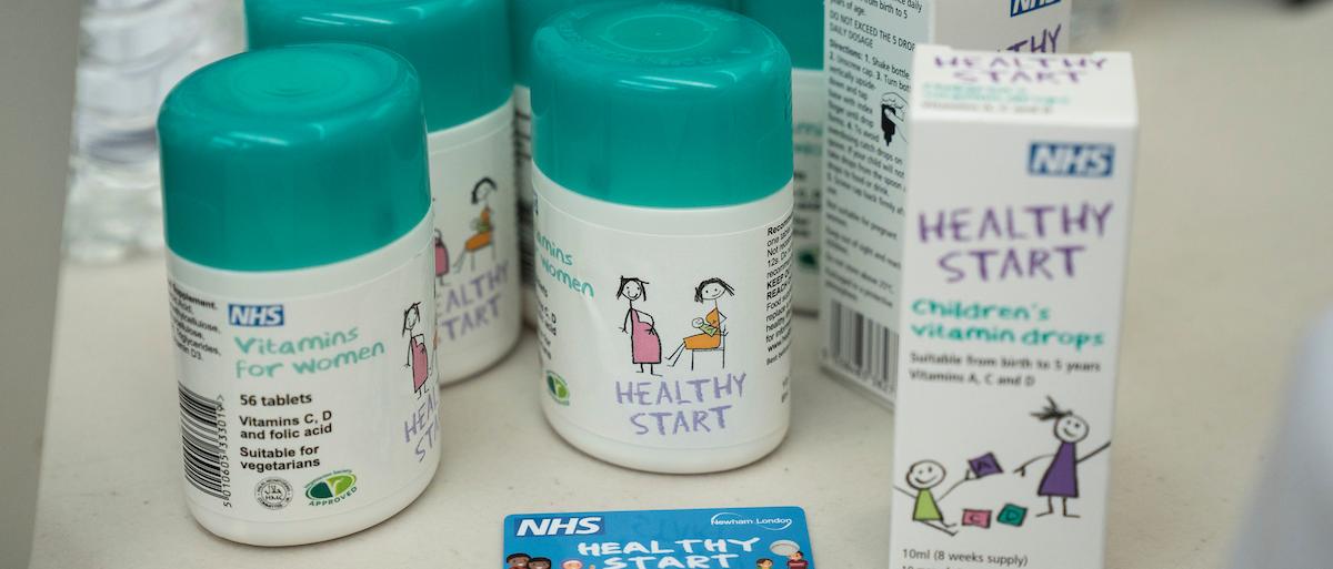 Table with bottles of healthy start vitamins on top. The bottles are white with a turquoise cap.