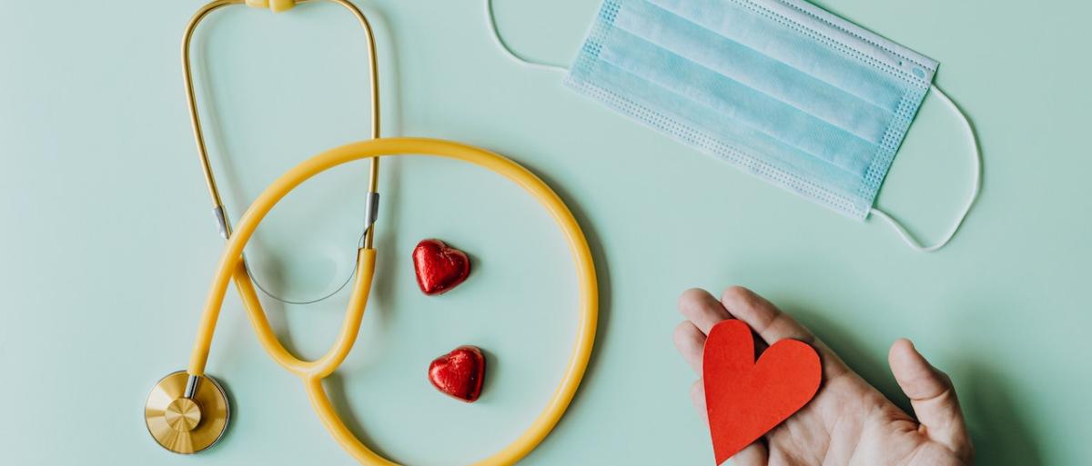 Someone holding a fabric heart, a disposable face mask and yellow stethoscope