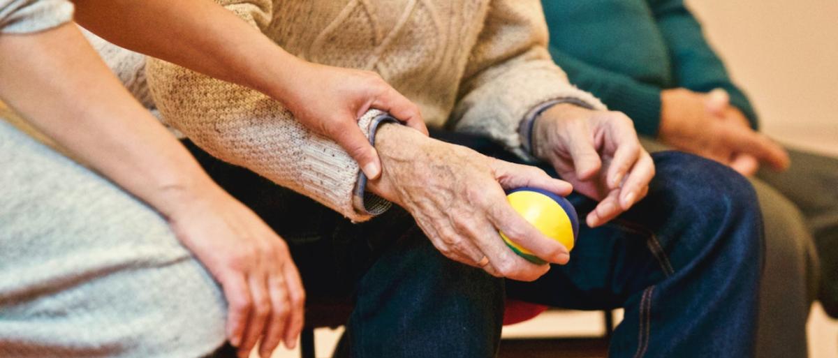 Older person holding a soft ball sitting next to a care worker