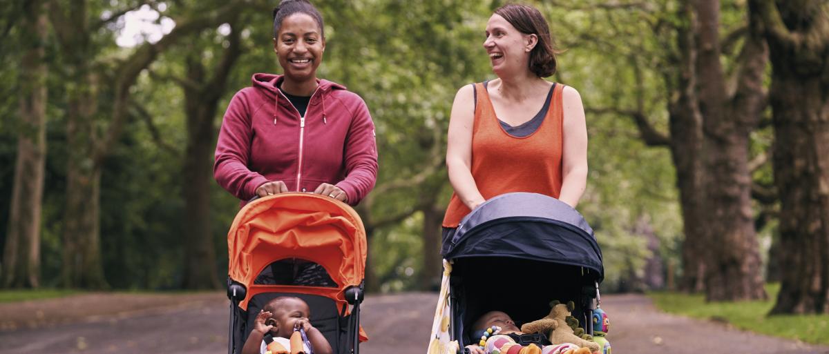 2 mothers taking a walk through the garden with their babies 