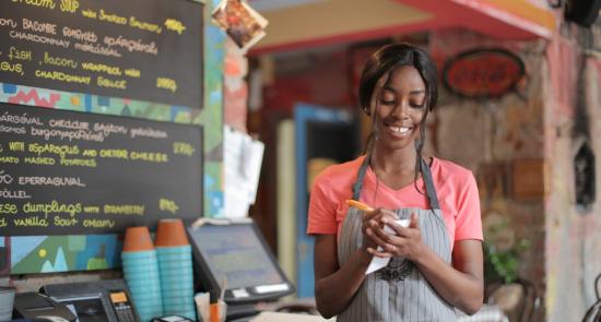 Woman working in a café writing notes on her notepad and smiling